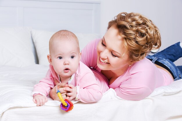 Portrait de l'heureuse jeune mère attactive couchée avec son bébé sur le lit à la maison