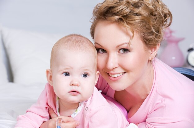 Portrait de l'heureuse jeune mère attactive couchée avec son bébé sur le lit à la maison