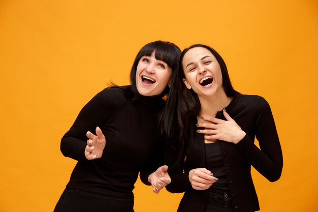 Un portrait d'une heureuse mère et fille souriante au studio sur fond d'or. Couleurs à la mode. Concept d'émotions positives humaines et d'expressions faciales