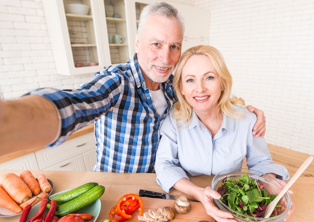 Portrait, heureux, couple senior, prendre, selfie, pendant, préparation, salade cuisine