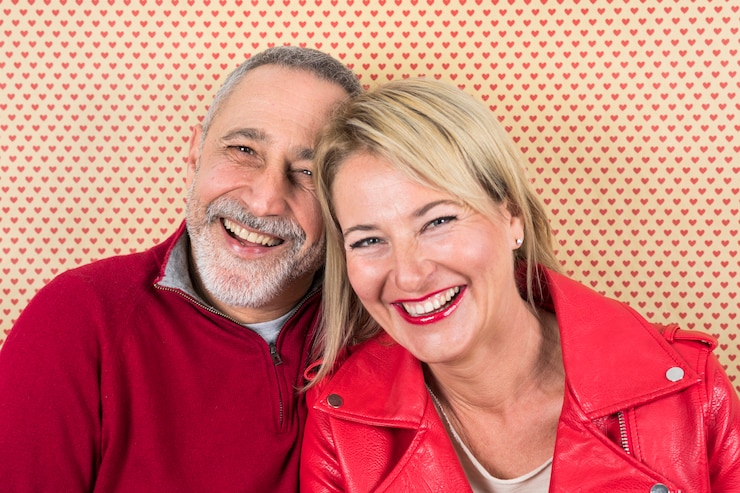 Photo gratuit portrait heureux du couple de personnes âgées contre le papier peint en forme de cœur