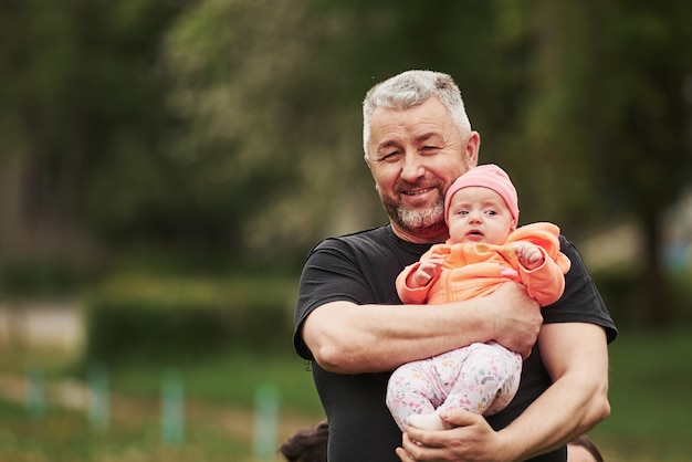 Portrait d'heureux grand-père barbu tenant l'enfant dans le parc