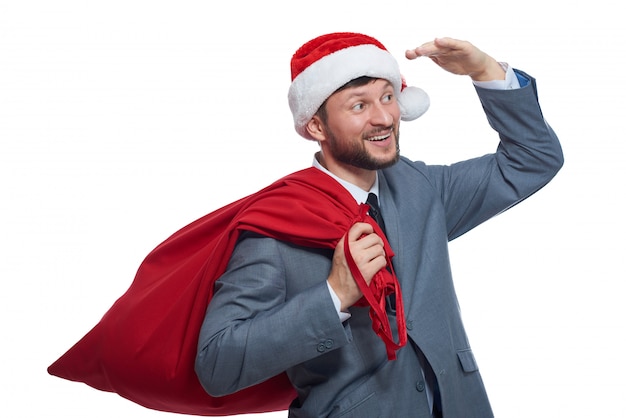 Portrait de l'heureux père Noël avec sac plein rouge avec des cadeaux, tenant la main sur les yeux