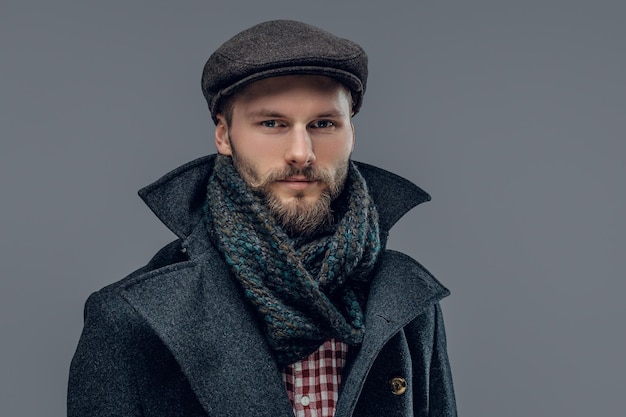 Portrait d'un hipster barbu vêtu d'une veste grise et d'un bonnet de laine isolé sur fond gris.