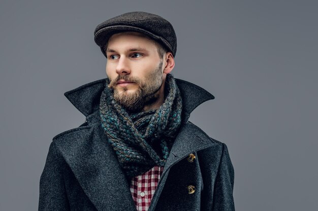 Portrait d'un hipster barbu vêtu d'une veste grise et d'un bonnet de laine isolé sur fond gris.