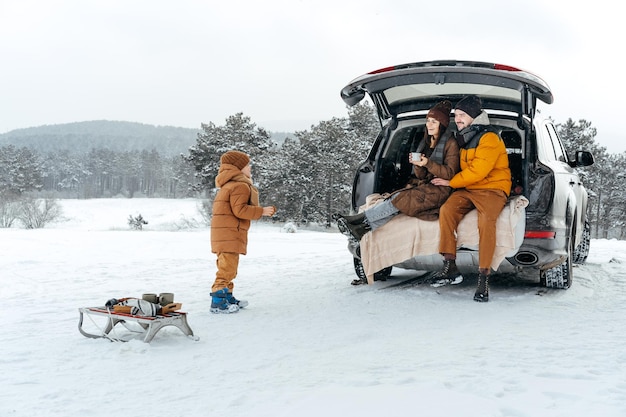 Portrait D'hiver D'une Famille Assise Sur Le Coffre D'une Voiture Profitant De Leurs Vacances En Forêt Photo Premium
