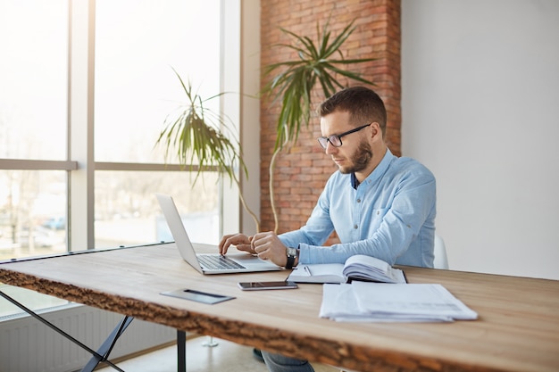 Portrait d'un homme adulte sérieux, directeur d'entreprise assis dans un bureau confortable, vérifiant les bénéfices de l'entreprise sur un ordinateur portable