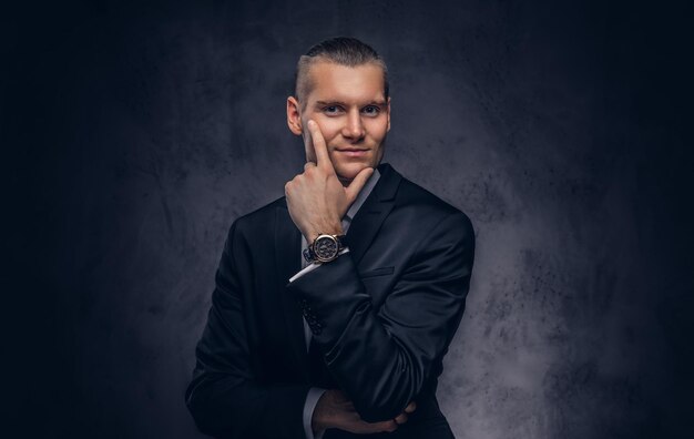 Un portrait d'un homme d'affaires élégant et souriant sur un fond sombre.