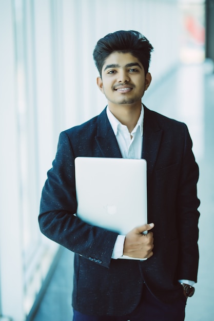 Photo gratuite portrait d'homme d'affaires indien heureux à l'aide d'un ordinateur portable au bureau