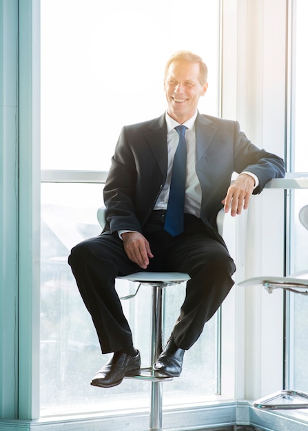 Photo gratuite portrait d'un homme d'affaires mature heureux assis sur un tabouret