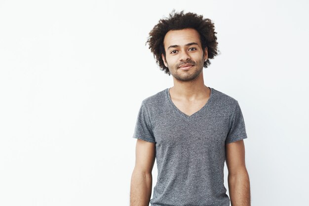 Portrait d'un homme africain fort et beau souriant posant sur un mur blanc. Étudiant ou propriétaire de magasin confiant.