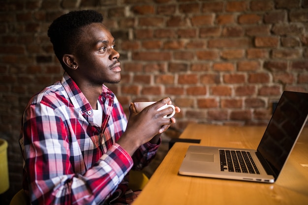 Photo gratuite portrait d'un homme afro-américain boire du café et travailler sur un ordinateur portable au café