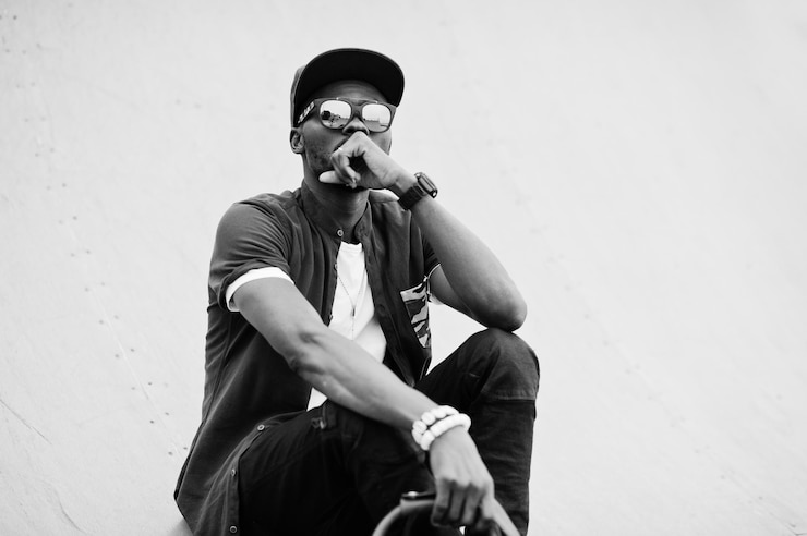 Photo gratuit portrait d'un homme afro-américain élégant assis portant des lunettes de soleil et une casquette avec sac à main en plein air street fashion black man