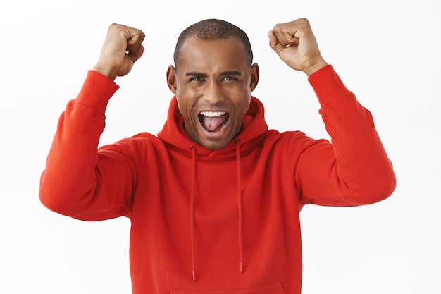 Portrait d'un homme afro-américain excité et joyeux qui lève les mains en triomphe, criant oui oui en regardant un match de sport, un pari gagnant