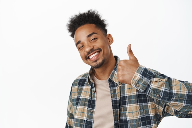 Photo gratuite portrait d'un homme afro-américain heureux souriant satisfait, dites oui, montrant le pouce vers le haut en signe d'approbation, encouragez-vous à faire du bon travail, louez un bon choix, fond blanc