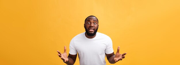 Portrait d'un homme afro-américain avec les mains levées sous le choc et l'incrédulité isolé sur fond jaune