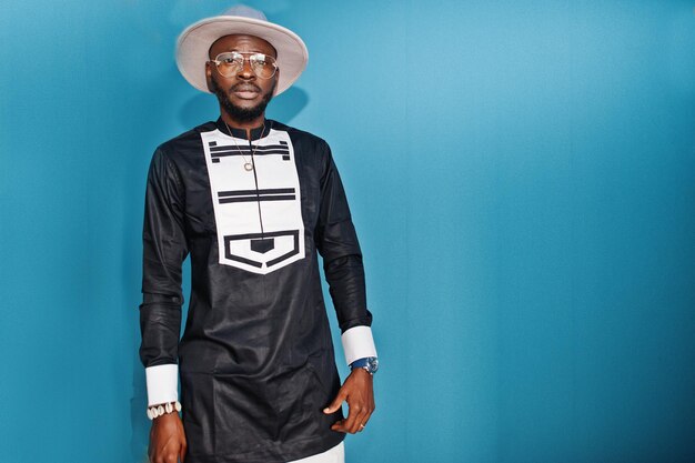 Portrait d'un homme afro-américain noir élégant au chapeau et lunettes sur fond bleu