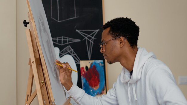 Portrait d'un homme afro-américain utilisant un crayon pour créer un croquis de dessin, assistant à un atelier artistique pour développer des compétences créatives en classe. Apprentissage d'une nouvelle activité contemporaine. Prise de vue à main levée