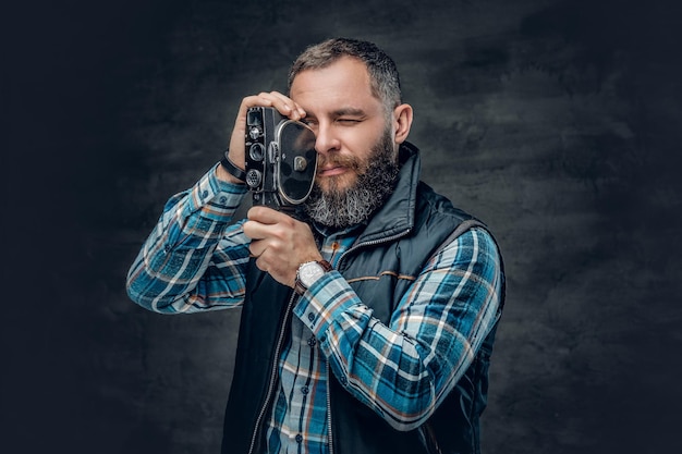 Portrait d'un homme d'âge moyen barbu tenant une caméra vidéo vintage de 8 mm sur fond gris.
