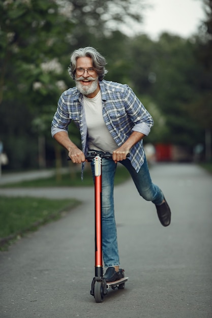 Portrait d'un homme âgé avec scooter dans un parc d'été