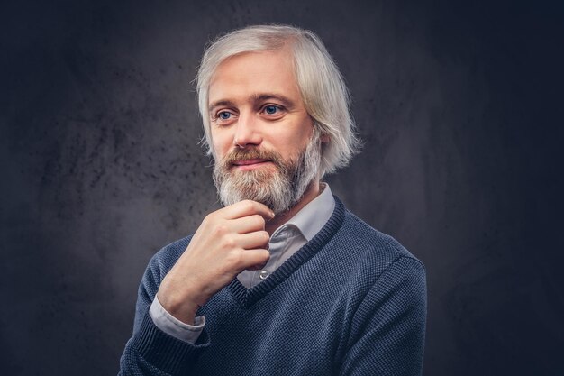 Portrait d'un homme âgé souriant avec une barbe grise isolée sur un fond sombre.