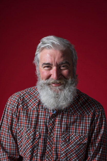 Portrait, homme aîné, barbe grise, regarder appareil-photo, contre, toile de fond rouge