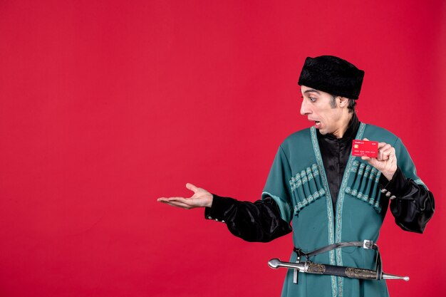 Portrait d'un homme azéri en costume traditionnel tenant une carte de crédit sur l'argent de printemps rouge couleur novruz ethnique