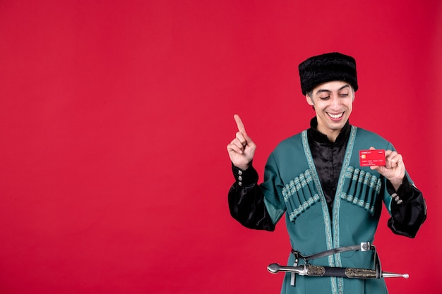 Portrait d'un homme azéri en costume traditionnel tenant une carte de crédit sur la couleur ethnique du printemps rouge novruz