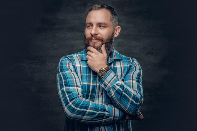 Portrait d'un homme barbu d'âge moyen sérieux vêtu d'une chemise en flanelle à carreaux sur fond gris.