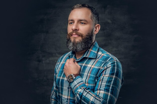 Portrait d'un homme barbu d'âge moyen sérieux vêtu d'une chemise en flanelle à carreaux sur fond gris.