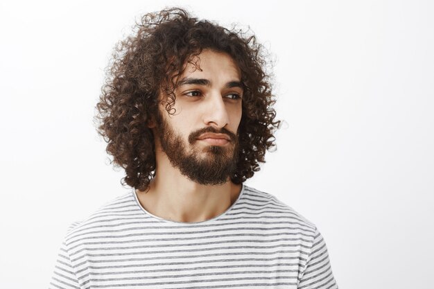 Portrait d'homme barbu attrayant deamy intelligent aux cheveux bouclés, regardant à droite tout en pensant ou en espaçant avec un léger sourire