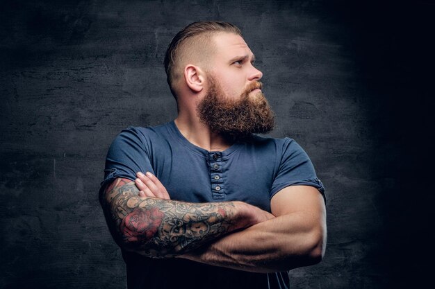 Portrait d'un homme barbu brutal aux bras croisés tatoués.