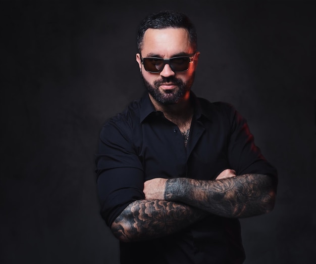 Photo gratuite portrait d'un homme barbu brutal en lunettes de soleil avec des tatouages sur les bras et le cou.