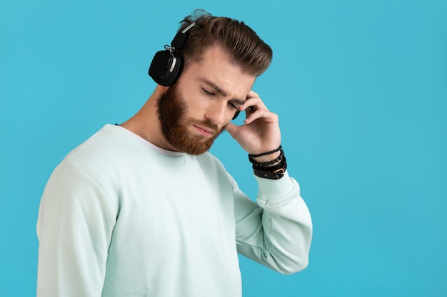 Portrait d'homme barbu, écouter de la musique sur des écouteurs sans fil sur bleu