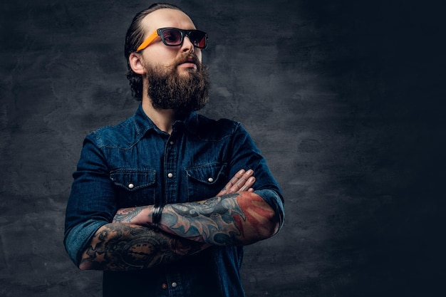 Portrait d'homme barbu à lunettes de soleil avec bras croisés tatoués.