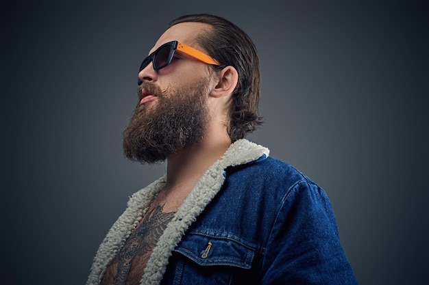 Photo gratuite portrait d'homme barbu à lunettes de soleil avec tatouage sur une poitrine portant une veste en jean.