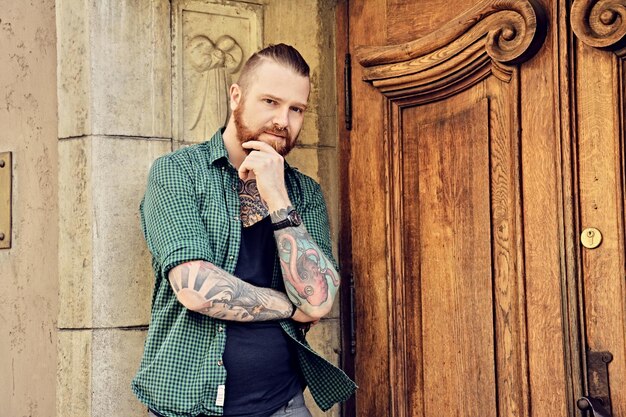 Portrait d'homme barbu rousse avec les bras croisés sur la vieille porte en bois massive.