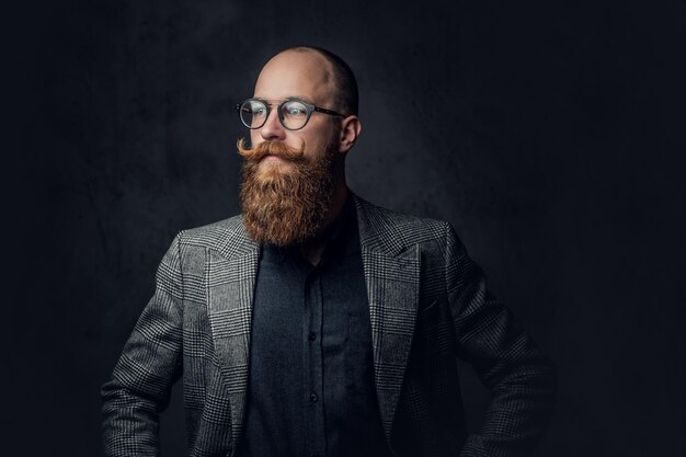 Portrait d'homme barbu rousse à lunettes vêtu d'un élégant costume de laine sur fond gris.