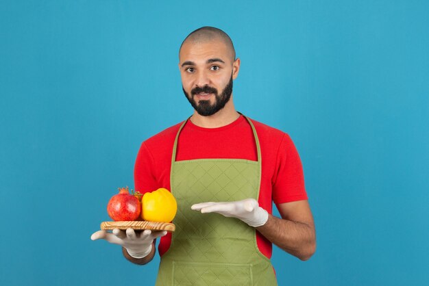 Portrait d'un homme barbu en tablier tenant une planche en bois de fruits frais.