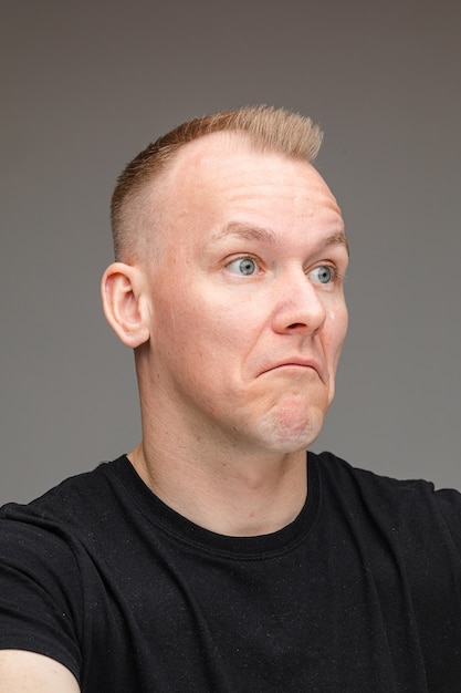 Portrait d'un homme caucasien blond en noir regardant loin avec une expression faciale incertaine montrant l'incertitude et la confusion.