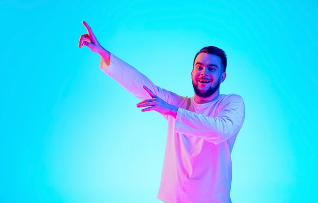 Portrait de l'homme caucasien isolé sur fond bleu studio en néon. Beau modèle masculin. Concept d'émotions humaines, expression faciale, ventes, publicité. Copyspace pour l'annonce.