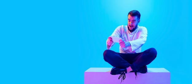 Portrait de l'homme caucasien isolé sur fond bleu studio en néon. Beau modèle masculin. Concept d'émotions humaines, expression faciale, ventes, publicité. Copyspace pour l'annonce.