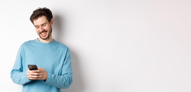 Portrait d'homme caucasien moderne avec barbe portant des vêtements décontractés lisant l'écran du smartphone et smi