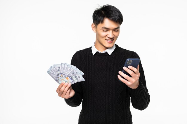 Portrait d'un homme chinois excité avec téléphone en mains montrant de nombreux billets isolés sur mur blanc