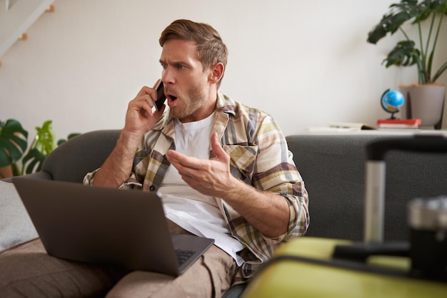 Photo gratuite portrait d'un homme en colère se disputant au téléphone a l'ordinateur portable ouvert sur son ordinateur portable est assis près de la valise