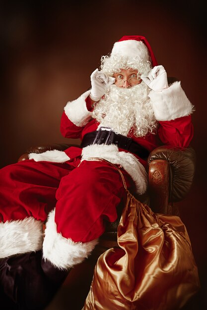 Portrait d'homme en costume de père Noël avec une barbe blanche luxueuse, un chapeau du père Noël et un costume rouge au rouge