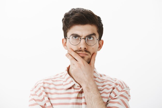 Portrait d'un homme déterminé et créatif avec une moustache drôle, se frottant le menton, levant les yeux tout en pensant, inventant une idée ou un concept, essayant de résoudre un problème mathématique difficile, faisant des calculs