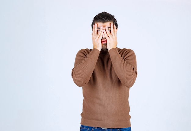 Portrait d'un homme effrayé couvrant son visage de paumes et regardant à travers les doigts isolés