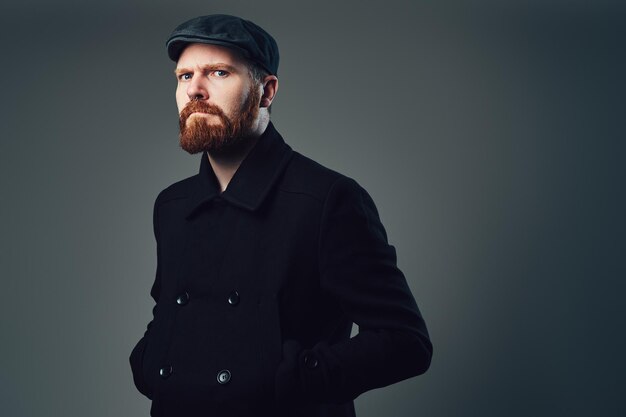 Photo gratuite portrait d'homme élégant barbe rouge vêtu d'une casquette plate en tweed et d'une veste noire sur fond gris.