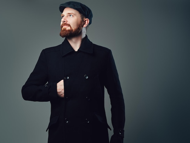 Portrait D'homme élégant Barbe Rouge Vêtu D'une Casquette Plate En Tweed Et D'une Veste Noire Sur Fond Gris.